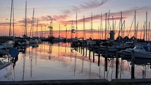 Een jachthaven met diverse boten afgemeerd, kalm water dat de boten en de luchtin de spiegelt, en een heldere horizon.