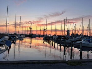 Un puerto deportivo con varias embarcaciones amarradas, agua tranquila que refleja las barcas y el cielo, y un horizonte despejado.
