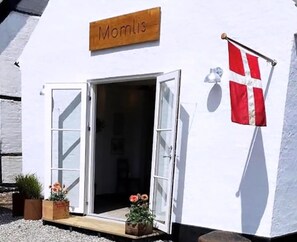 Un edificio con un letrero que dice 'Momlis', una bandera y dos macetas con plantas afuera.