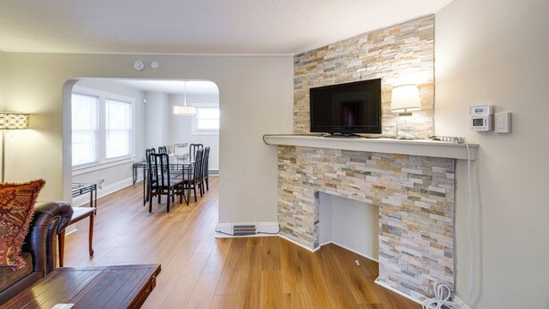 A living room with a stone fireplace, a flat-screen TV, and a dining area with chairs and a table. - 11 Mi to Dtwn Cleveland: Family Home w/ Yard (Garfield Heights)
