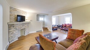 A spacious living room with a stone fireplace, a flat-screen TV, a sofa set, and a staircase leading to an upper level. - 11 Mi to Dtwn Cleveland: Family Home w/ Yard (Garfield Heights)