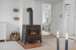 A room with a wood-burning stove, a basket of firewood, and two lit candles.
