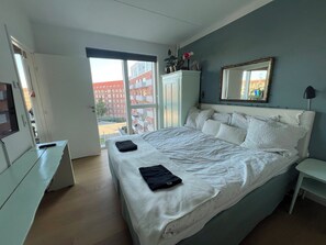 A bedroom with a bed, a desk, a wardrobe, a mirror, and a view of buildings outside. - New York Style appartment central Copenhagen (København)