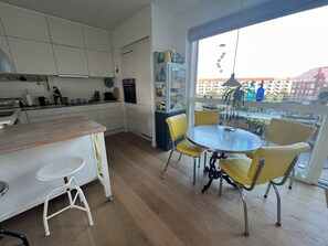 A modern kitchen with white cabinets, a wooden countertop, and a dining area with yellow chairs and a round table. - New York Style appartment central Copenhagen (København)
