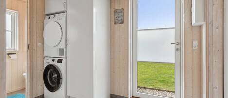 Uma lavanderia com máquina de lavar e secadora, uma porta que dá para o exterior e uma pequena placa na parede.