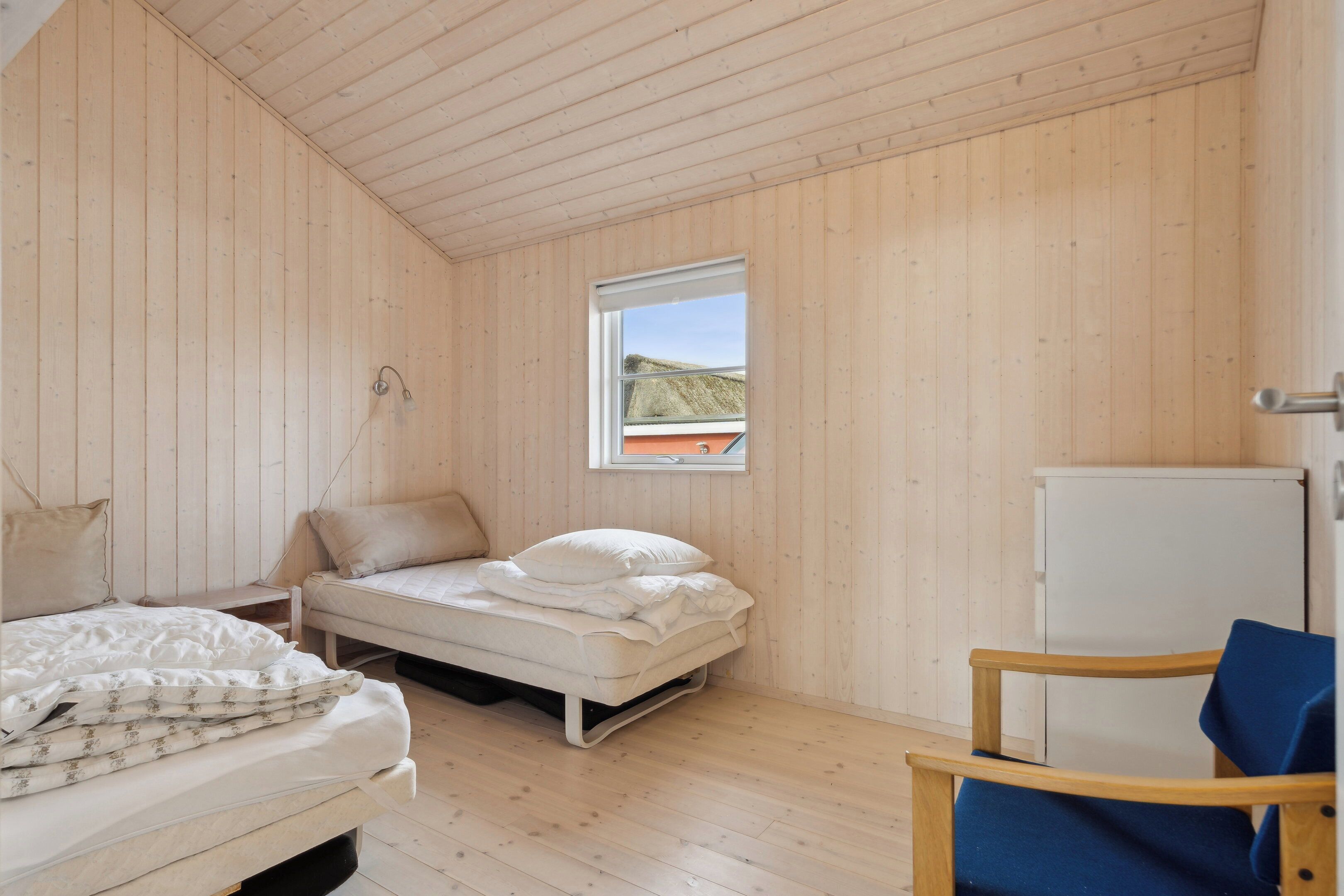 Ein kleiner Raum mit Holzwänden, zwei Betten, einem Fenster und einem Stuhl.