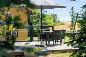 An outdoor patio with a table and chairs, surrounded by greenery and a yellow wall.