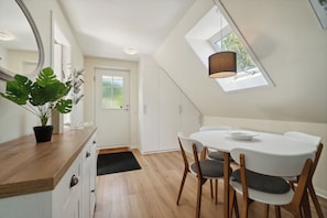 A modern kitchen with white cabinets, a wooden countertop, a dining table with chairs, a potted plant, and a skylight.