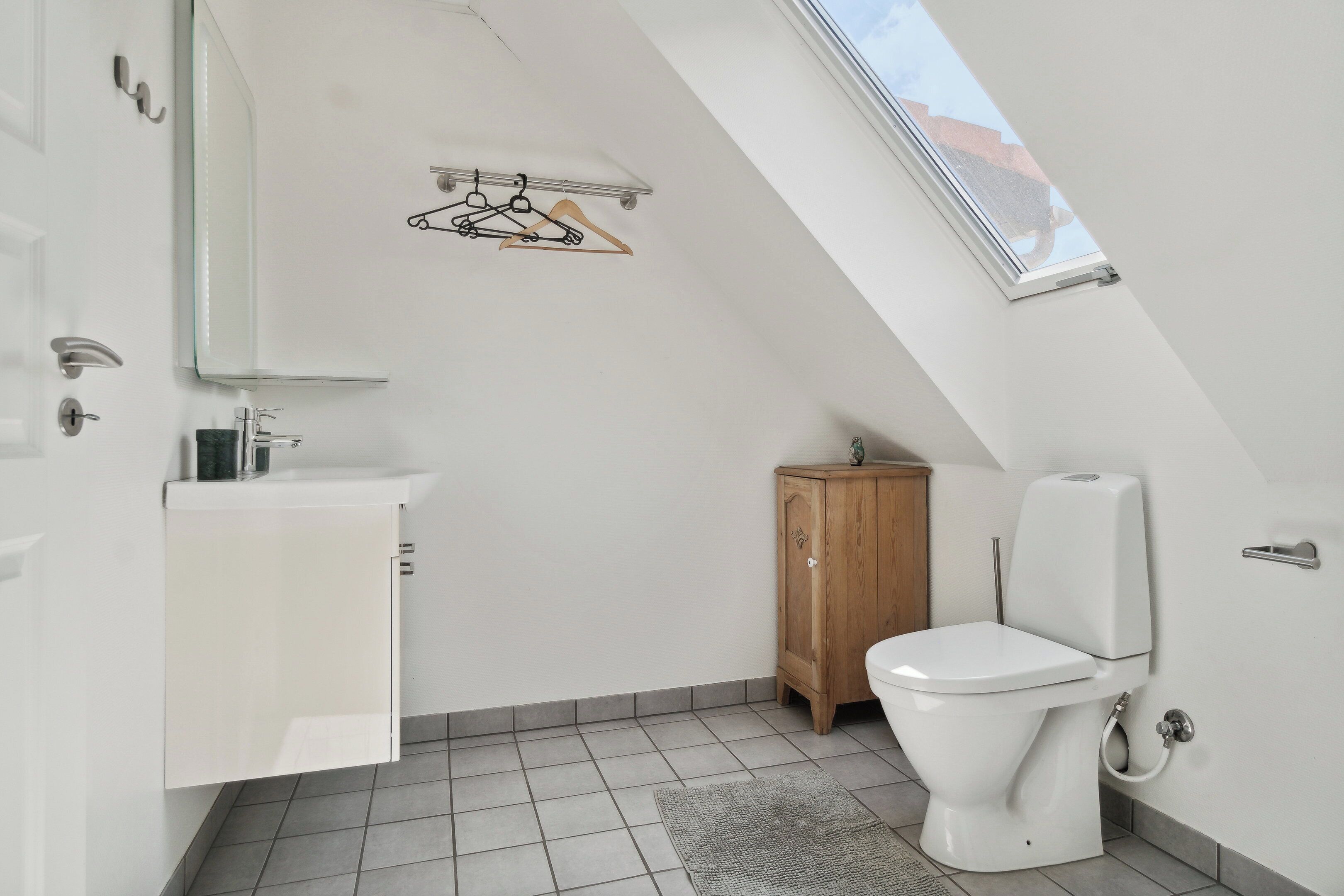 A small, modern bathroom with a skylight, a toilet, a wooden cabinet, and a white sink.