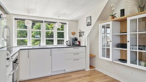 A modern kitchen with white cabinetry, a large window, and a wooden floor.