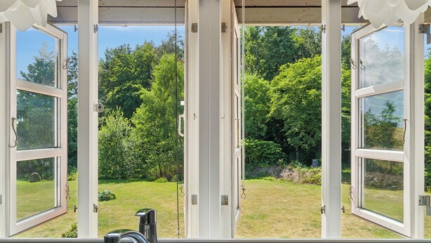 A kitchen with a sink and an open window overlooking a garden.