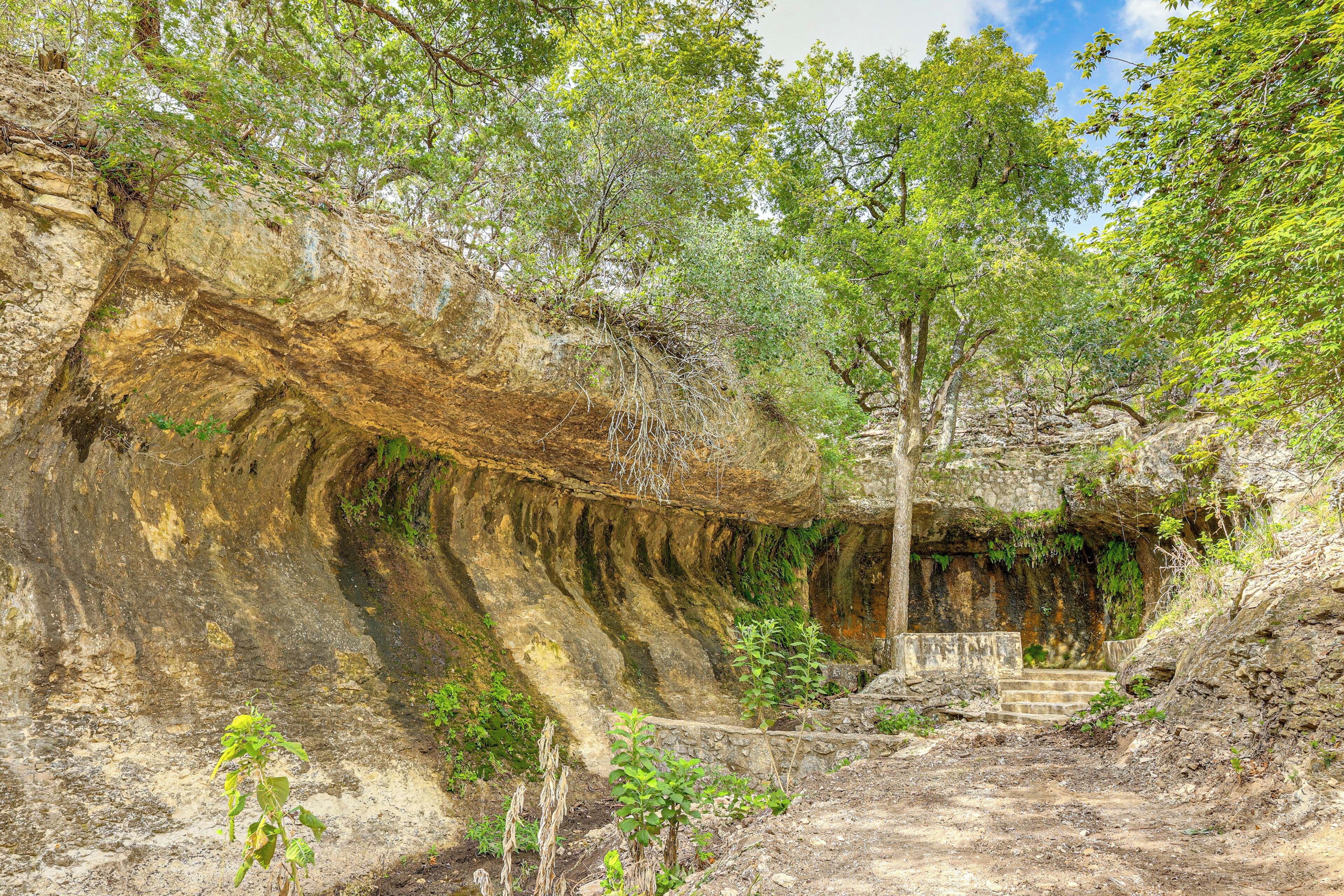A natural cave entrance with a dirt path leading inside, surrounded by trees and vegetation.
