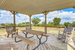 An outdoor wooden deck with picnic tables and chairs, surrounded by a metal fence and trees. - Fire Pit, Views: Peaceful Texas Hill Country Cabin (Tarpley)