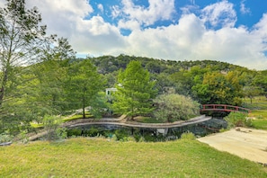 Un paysage paisible avec un étang, un pont rouge et une colline parsemée d’arbres.