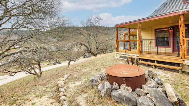 Un chalet rustique doté d’un porche en bois, d’un foyer en pierre et offrant une vue sur un paysage aride et vallonné.