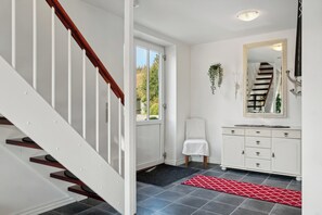Un escalier avec des rampes blanches et des marches en bois, un mur blanc orné d’un miroir et d’une armoire, et un tapis à motifs rouges sur le sol.
