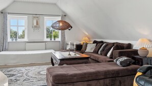 Ett mysigt rum med en brun soffa, ett träbord, en lampa och ett fönster med gardiner.