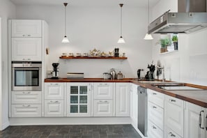 A modern kitchen with white cabinetry, a built-in oven, a coffee machine, and pendant lighting.