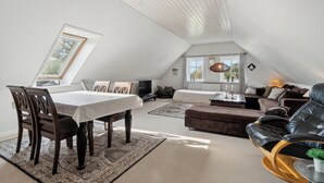Ett rum i loftstil med ett matbord, stolar, en soffa, en fåtölj och en tv.