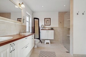 Une salle de bain équipée d’un double lavabo, de toilettes, d’une douche et d’un marchepied.