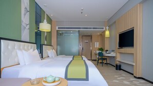 Habitación de hotel con una cama grande, un escritorio, una silla, un televisor y una pequeña mesa con tetera y taza.
