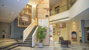 Un vestíbulo amplio con una escalera, una planta grande en maceta, zona de estar y exhibición de servicios.