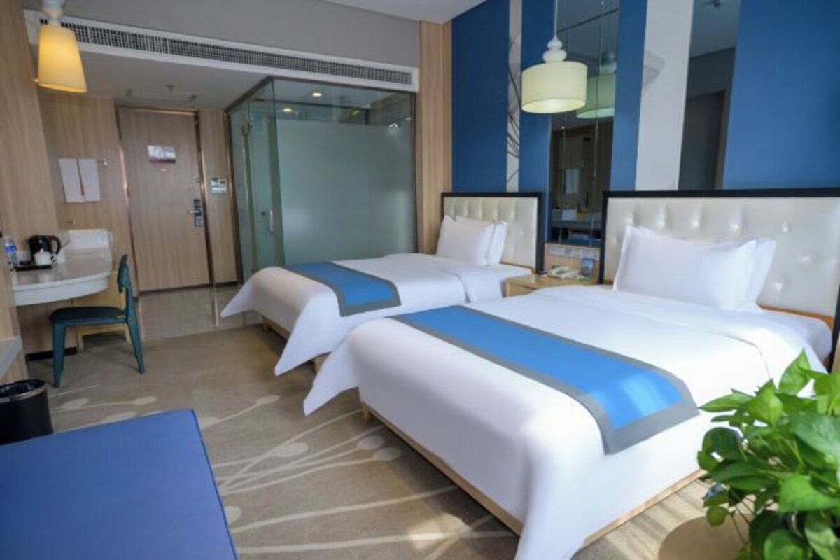 A hotel room with two beds, a desk, a chair, and a large window.