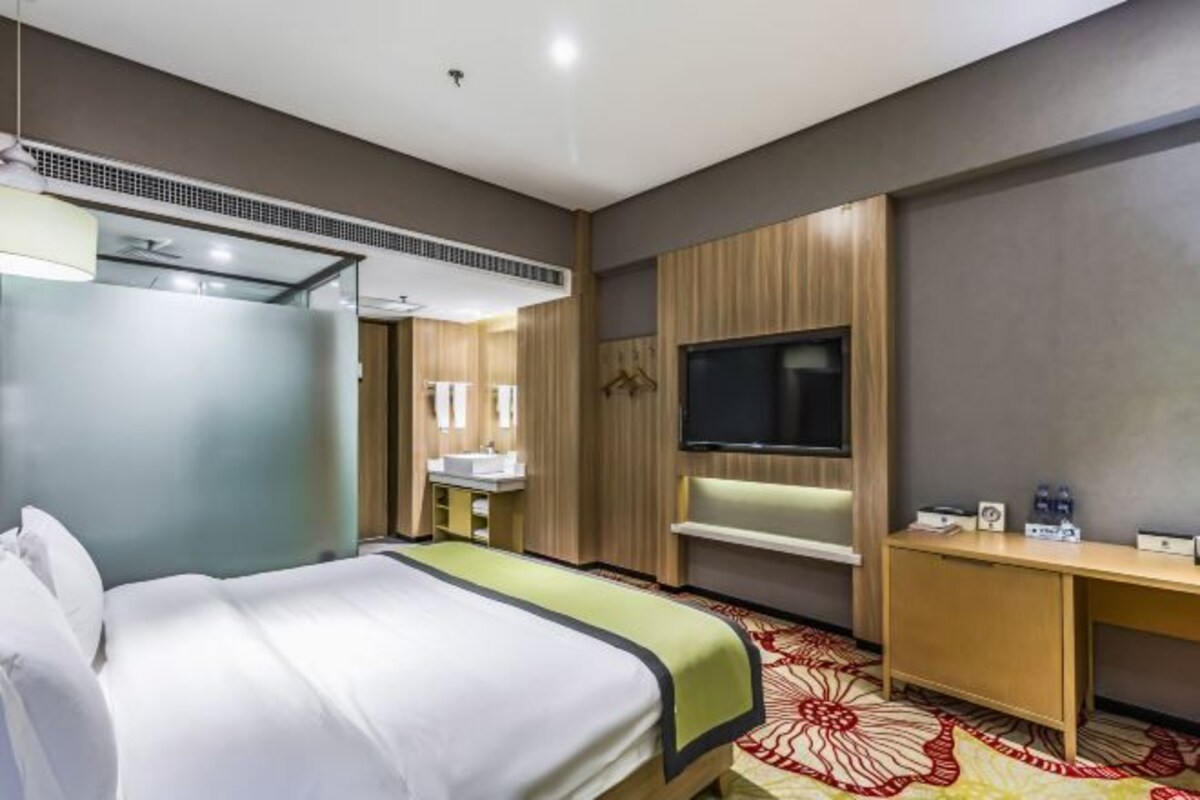 A hotel room with a bed, a TV, a desk, and a mirror.