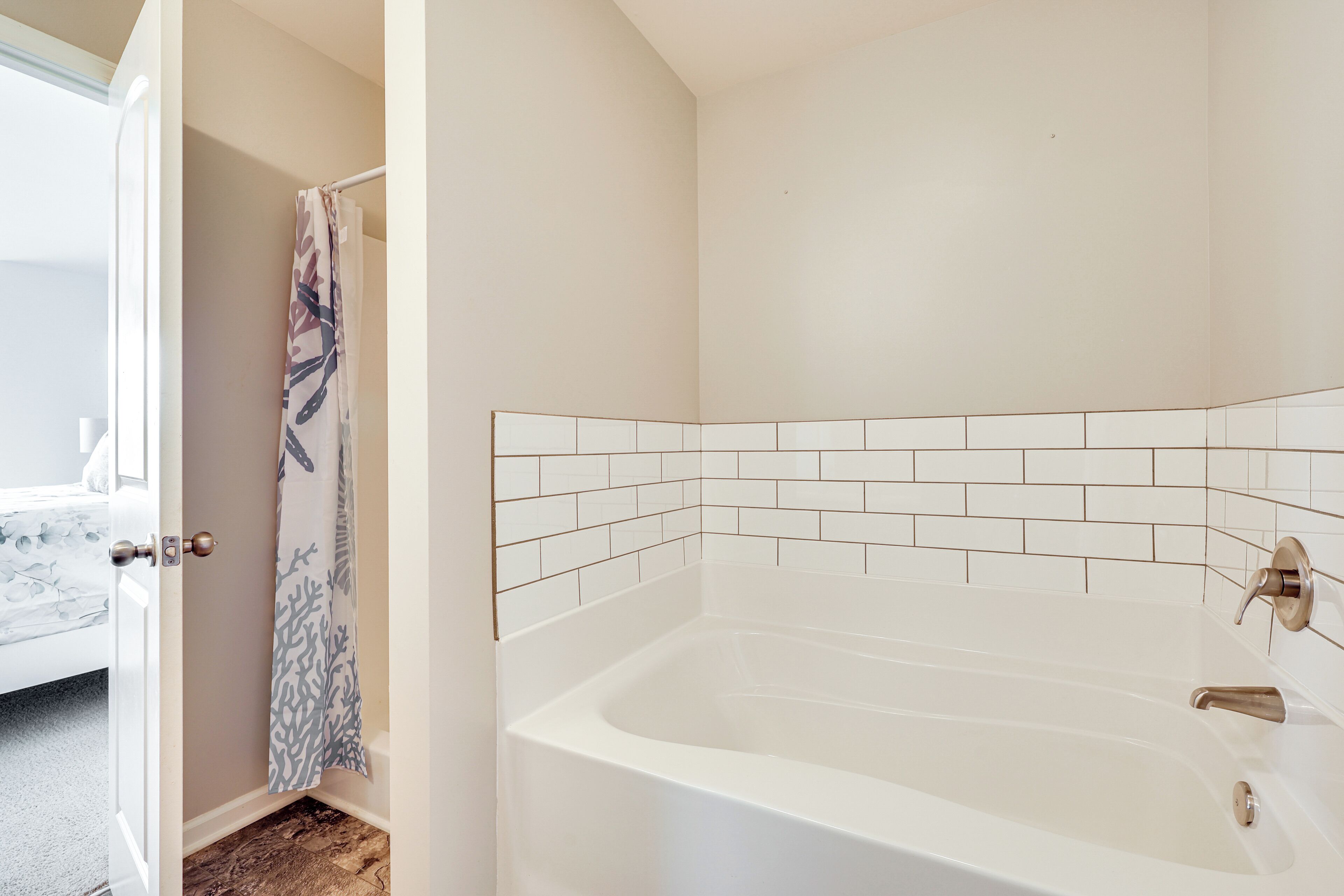 A bathroom with a white bathtub, a shower curtain, and a tiled wall.
