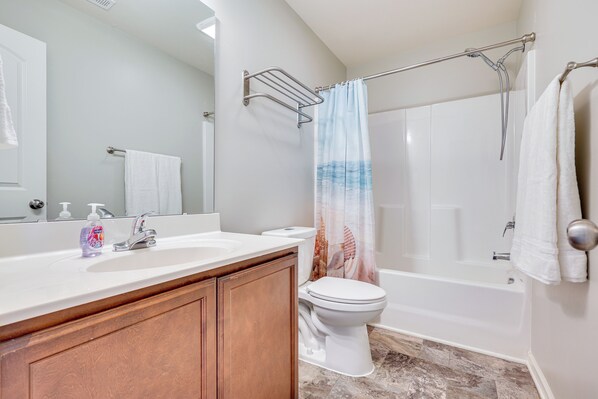 A bathroom with a white sink, wooden cabinets, a toilet, a bathtub, and a shower curtain. - 1 Mi to Ocean: Modern Carolina Beach Townhome (Carolina Beach)