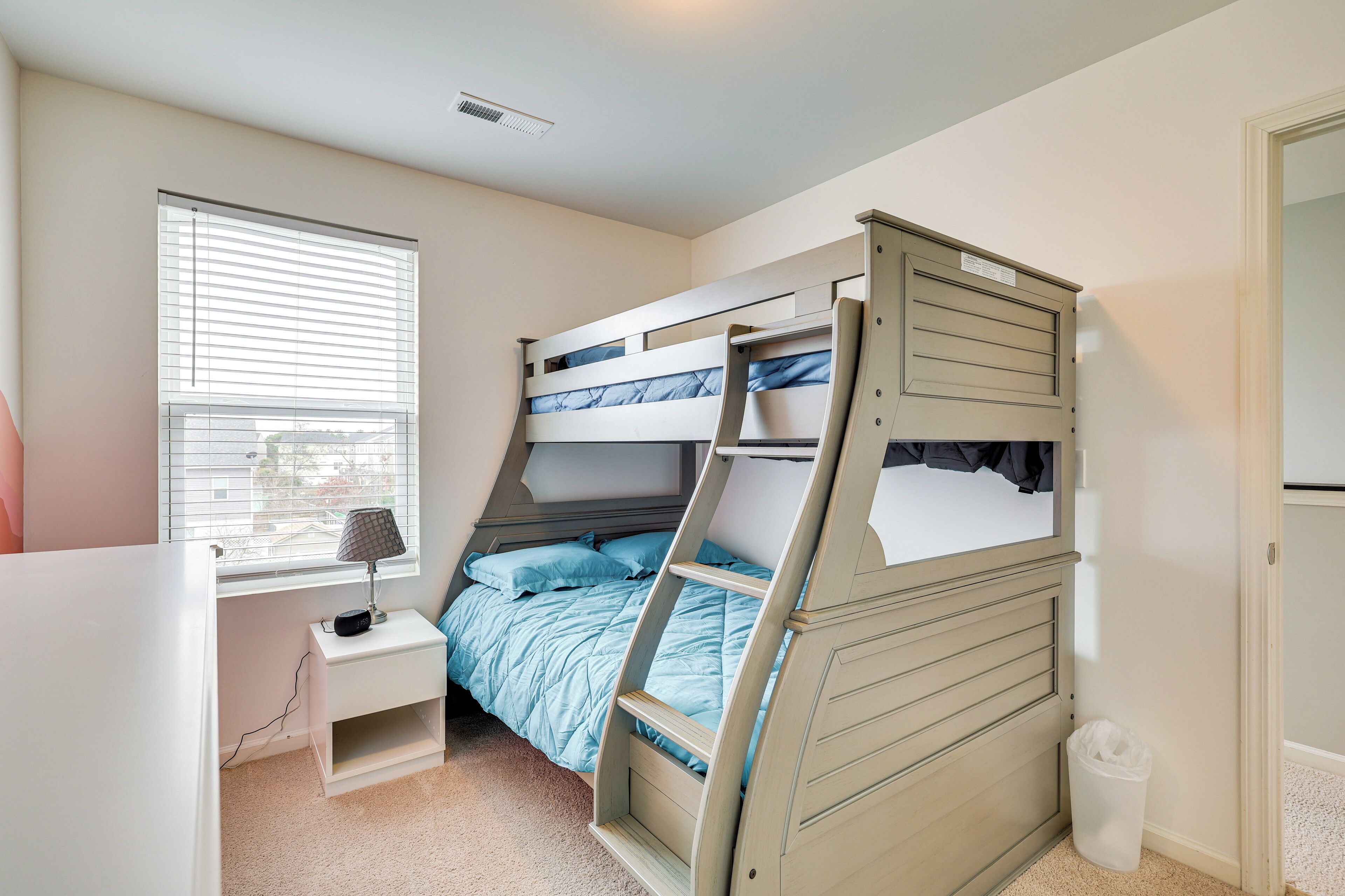 A bunk bed with a desk and lamp, a window with blinds, and a trash can.