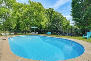 A swimming pool with a curved edge, surrounded by a fence, and trees in the background. - New Studio Walkable to Lake & Village w/ Pool! (Hammondsport)