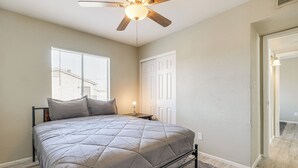 Une chambre à coucher comprenant un lit, un ventilateur de plafond, une fenêtre avec des stores, une porte et un tapis.