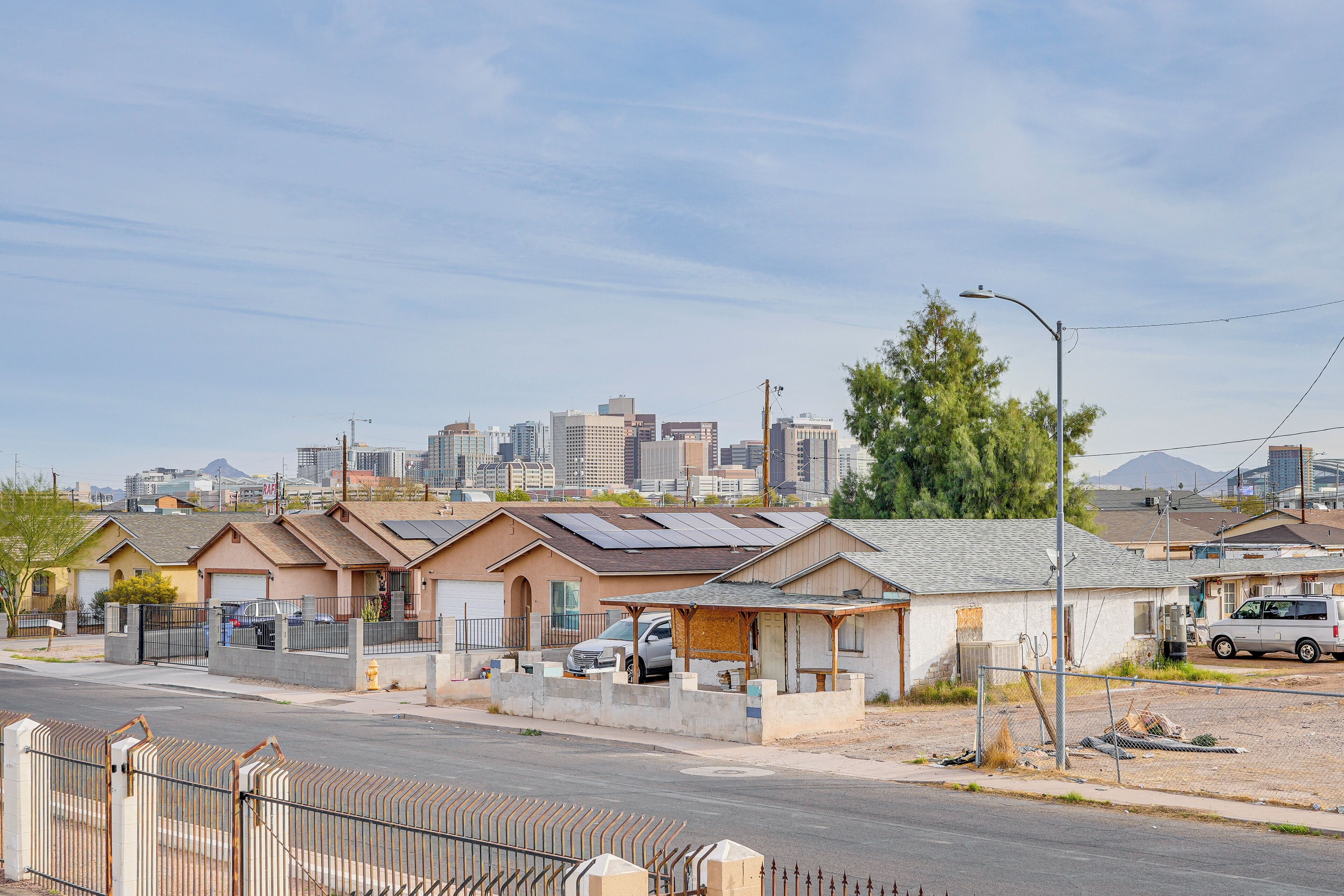 A row of single-story houses with attached garages, a street in the foreground, and a city skyline in the background.