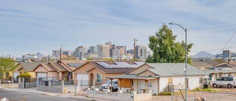 A row of single-story houses with attached garages, a street in the foreground, and a city skyline in the background.