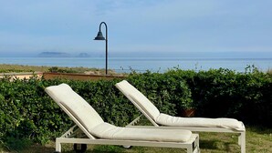 Dos sillones blancos con cojines, ubicados en un área verde con vistas al mar y a paisajes distantes.