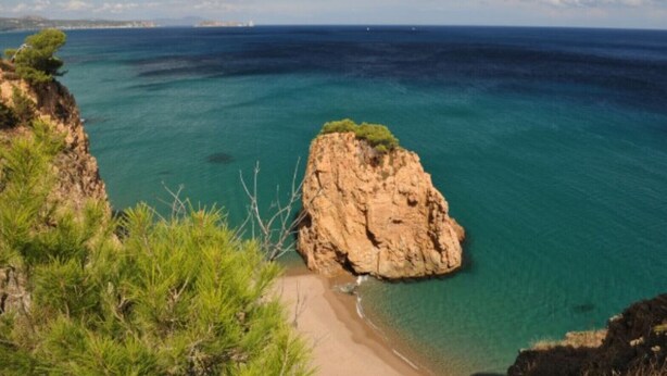 Un paisaje costero con un prominente afloramiento rocoso rodeado de aguas azules cristalinas y una playa de arena.