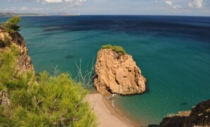 A coastal landscape with a prominent rocky outcrop surrounded by clear blue waters and a sandy beach.