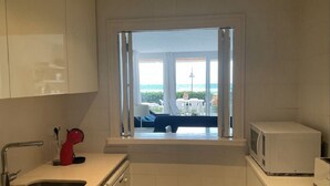 Una cocina con vistas al mar, un microondas blanco y un hervidor rojo.