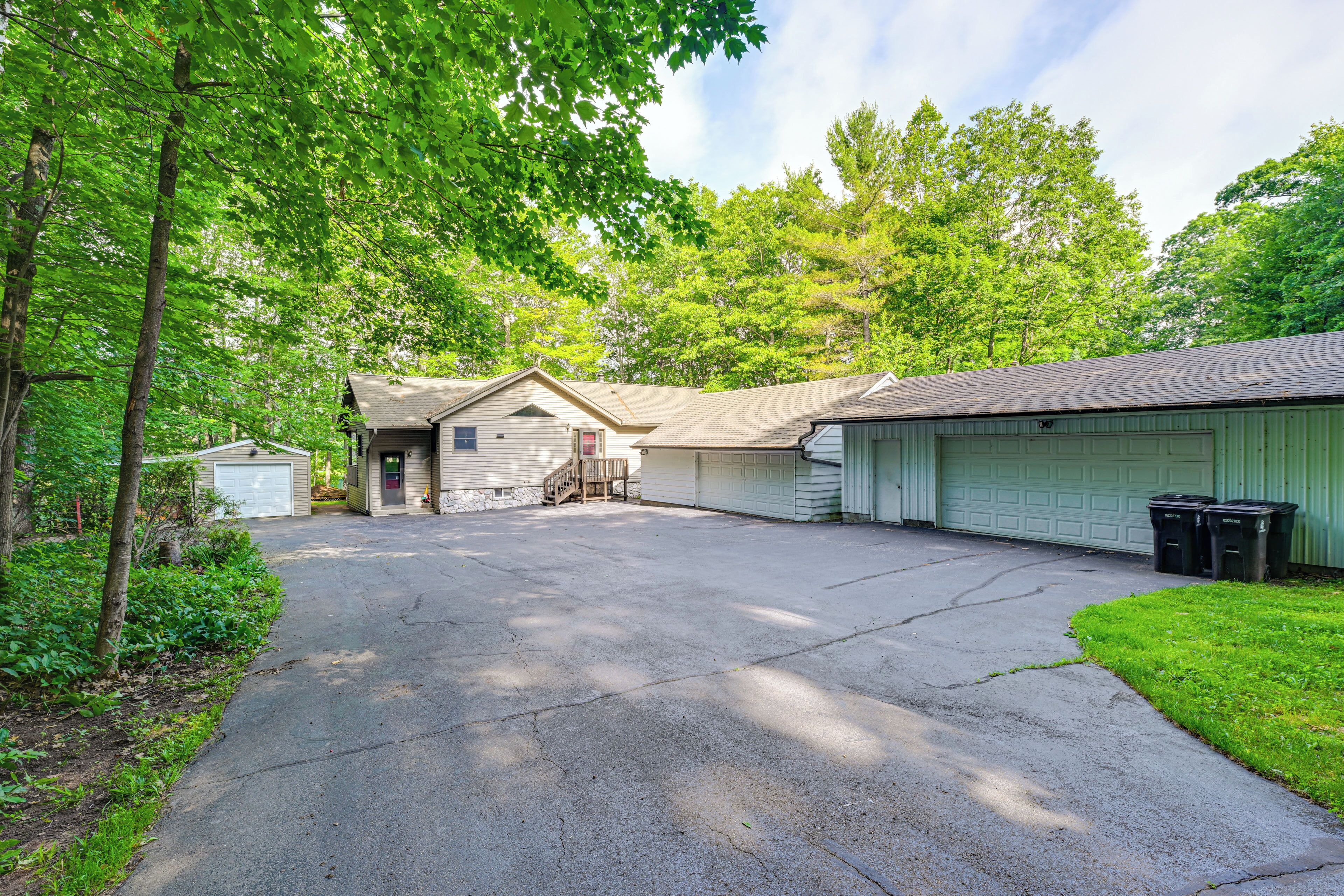 A residential driveway leading to a house with a garage, a small shed, and a covered area with trash bins.