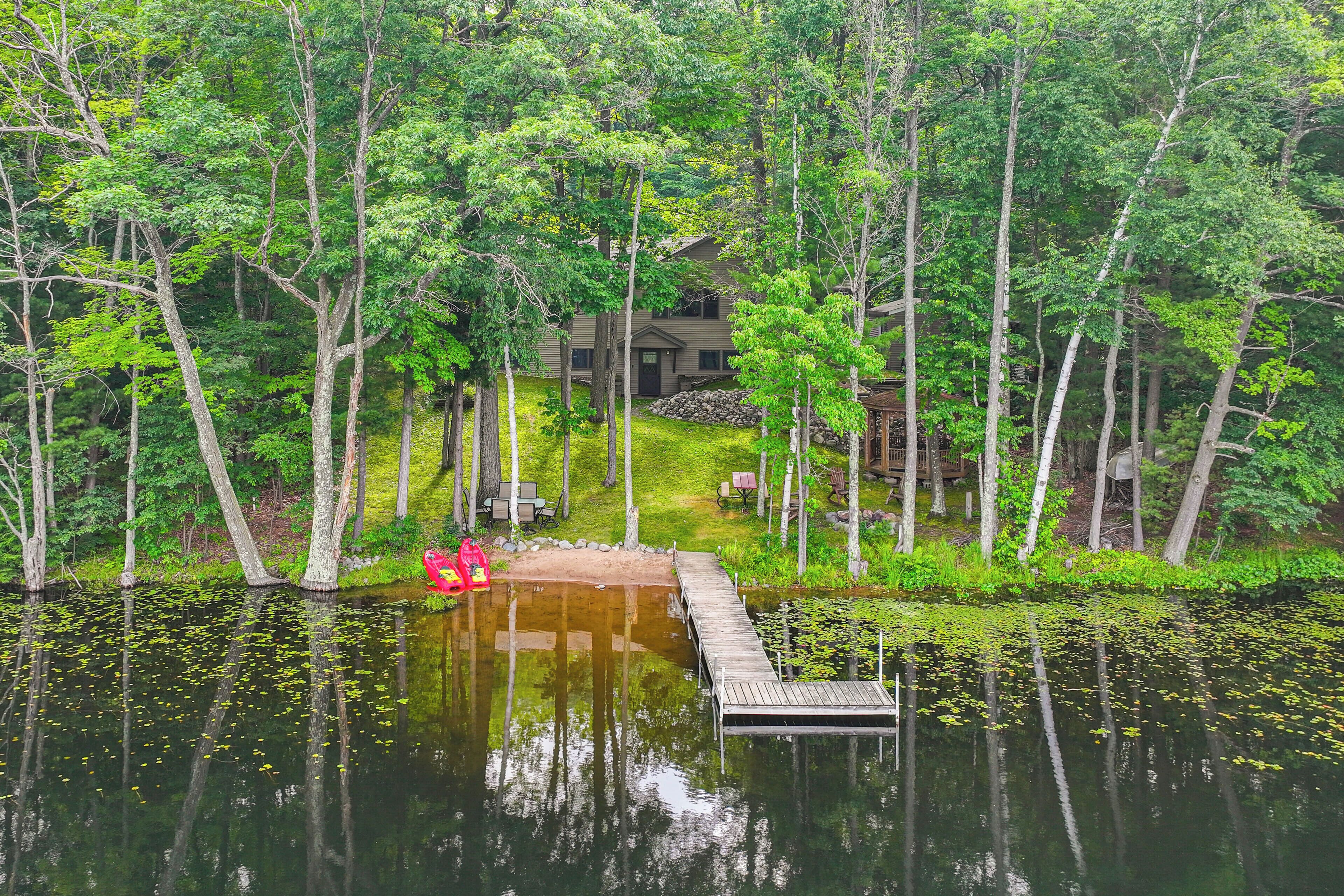 A lakeside cabin with a dock extending into the water, surrounded by dense trees.