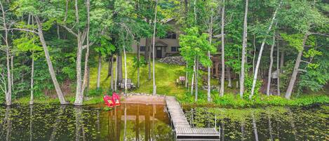 Un chalet au bord du lac, doté d’une jetée qui s’avance dans l’eau, et entouré d’une forêt dense.