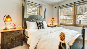 A bedroom with a bed, two bedside tables, lamps, and a window with a view of trees.
