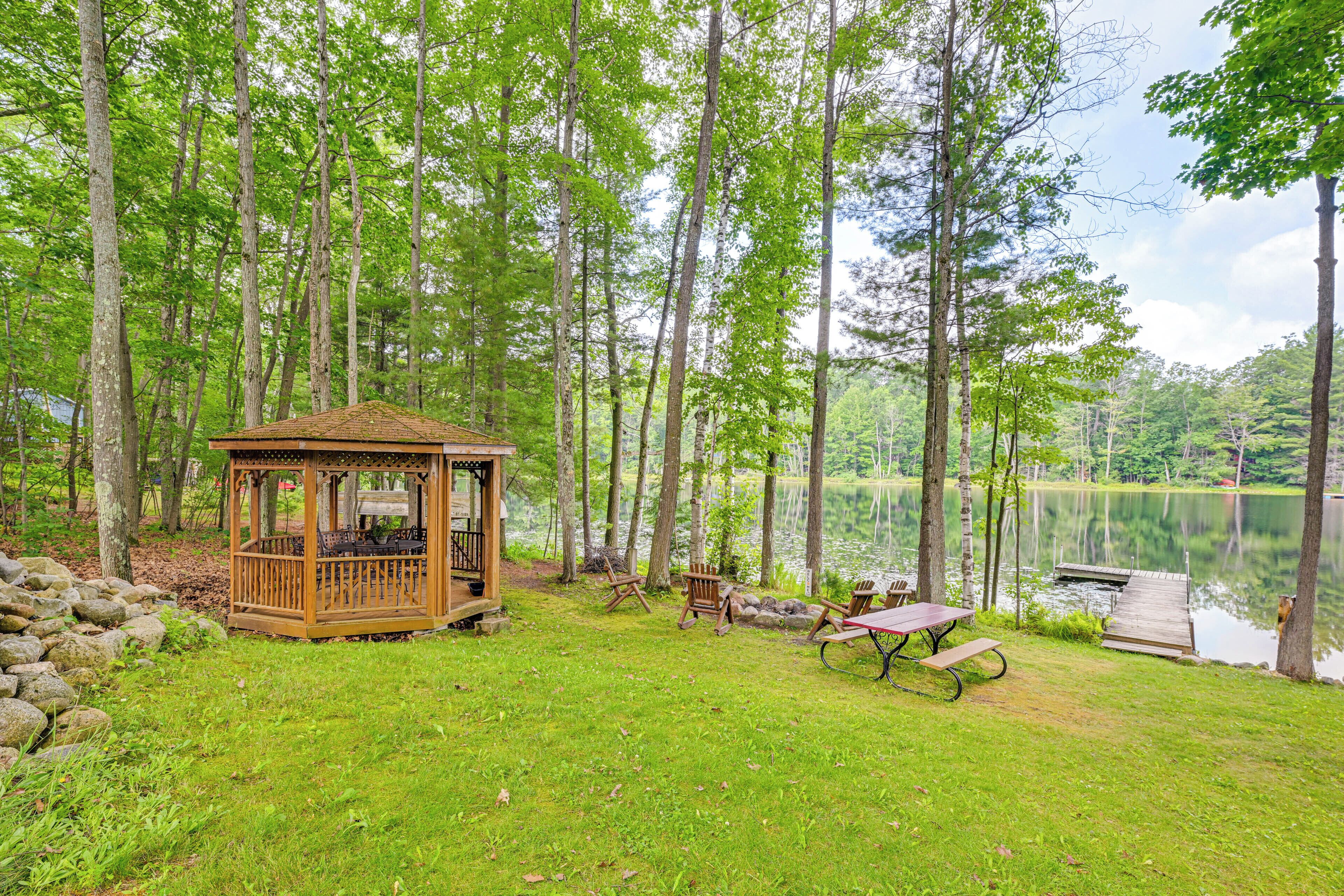 Un kiosque en bois avec une table de pique-nique et des chaises, situé au bord d’un lac.