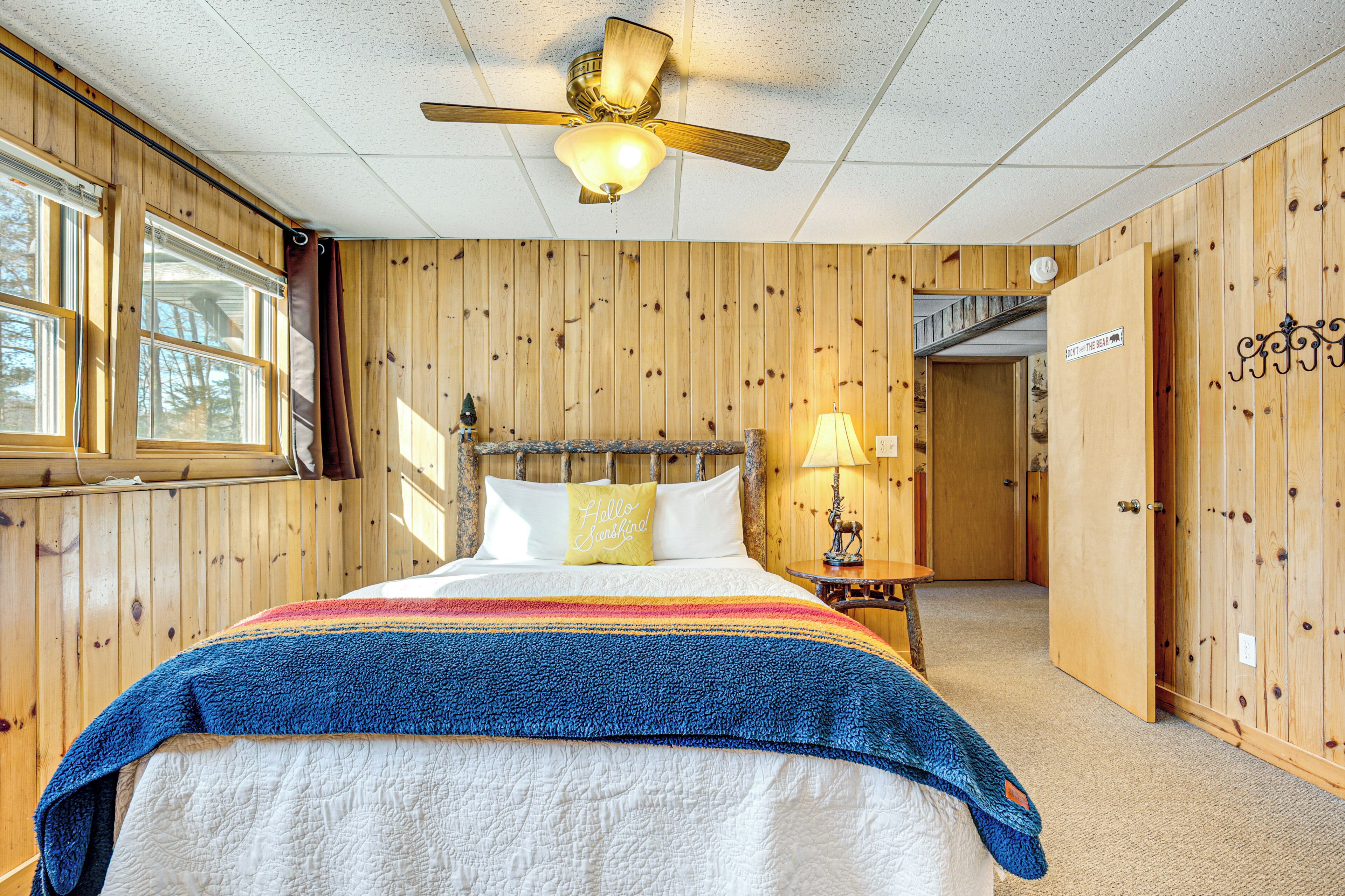 Habitación con paneles de madera, una cama, un ventilador de techo y una ventana.