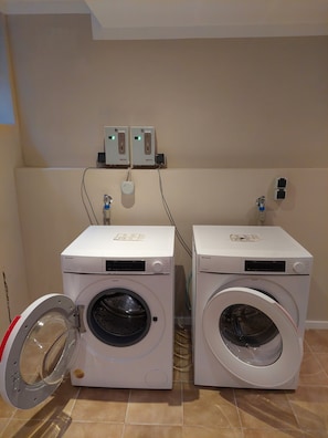 Two front-loading washing machines with control panels, connected to wall outlets, and a power outlet with a plug. - Apartment 'Bocksberg-Lodge' with Balcony and Wi-Fi (Hahnenklee/Goslar)