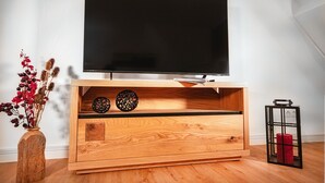 A wooden TV stand with a flat-screen TV, decorative plates, and a vase with red flowers.
