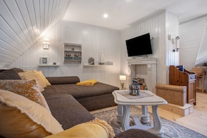A cozy living room with a sofa, a flat-screen TV, a fireplace, and a wooden cabinet.