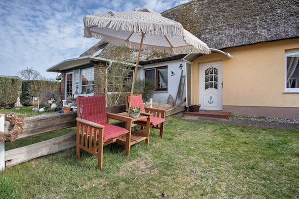 A house with a thatched roof, a wooden table and chairs, and a large umbrella.