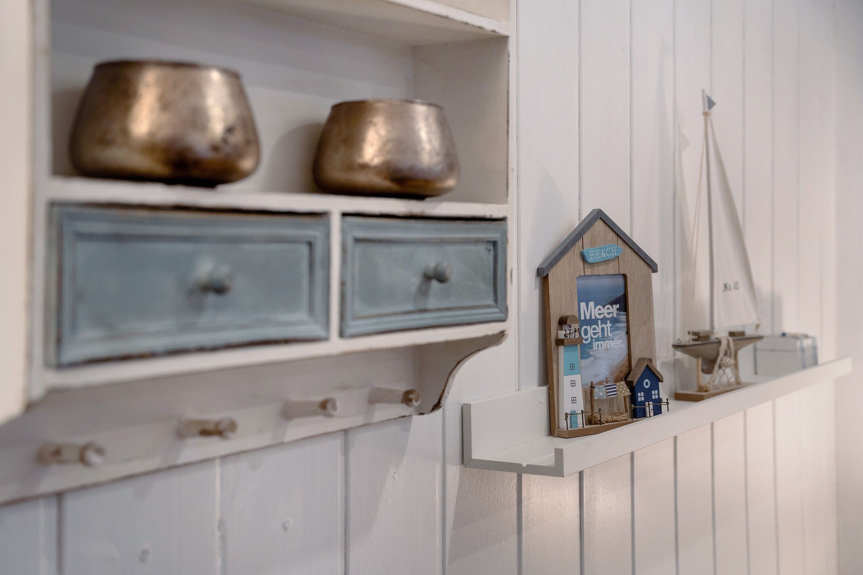 A white shelf with two metal bowls and a small wooden house model with a sign.